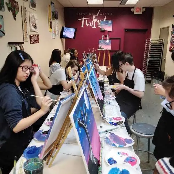 Group of people painting at long tables in an art studio with burgundy accent wall