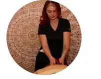 Woman in black shirt performing massage on a client's arm against a decorative circular backdrop