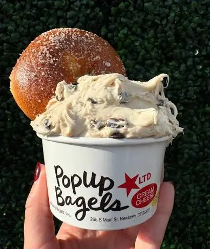 Large bagel stacked on top of a cup filled with cream cheese