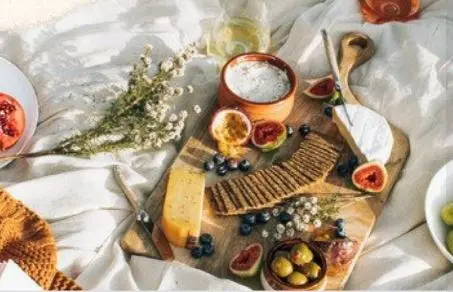 Overhead flatlay of wooden cutting boards with fresh citrus, olives, herbs, salt in a bowl, and scattered berries on white linens