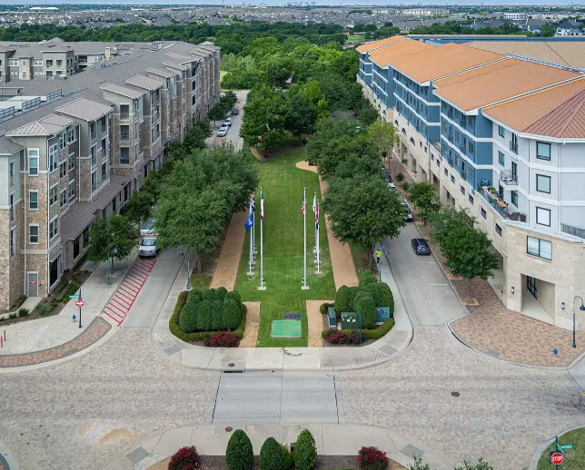 Aerial view of memorial park with green lawn, trees, and flagpoles surrounded by residential buildings