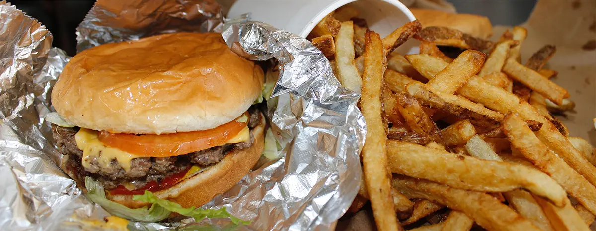 Burger wrapped in foil with lettuce and tomato, alongside golden french fries