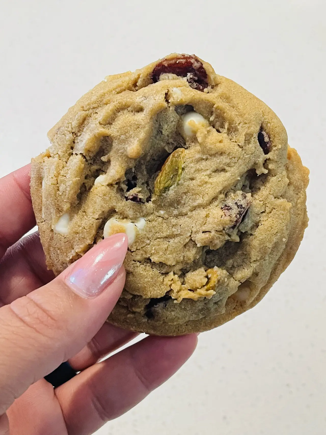 Hand holding a chunky cookie with chocolate chips and nuts, broken in half to show the interior texture