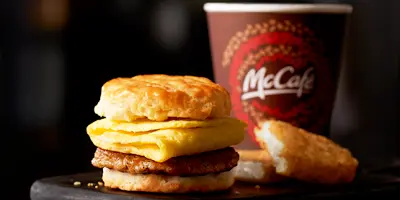 Breakfast sandwich with egg and cheese on biscuit, alongside coffee cup and hash brown