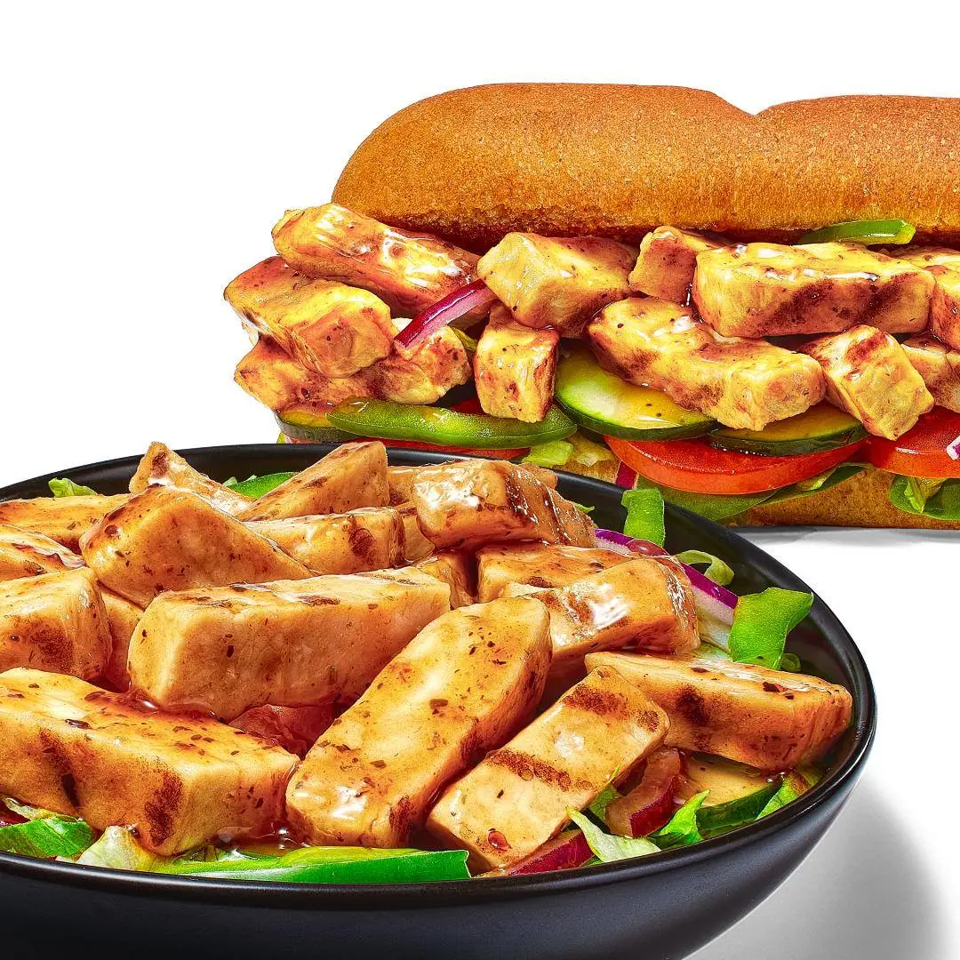 Crispy tofu strips with fresh vegetables and lettuce on a black plate, and a tofu sandwich on a toasted roll