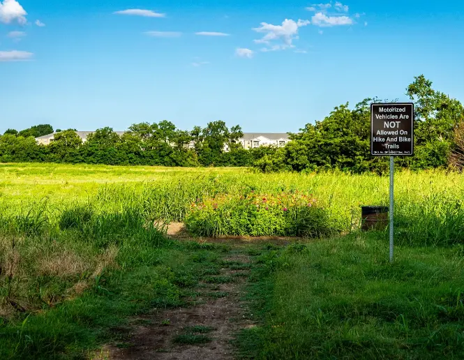 Open prairie with dirt trail, informational sign, and tree line under blue sky