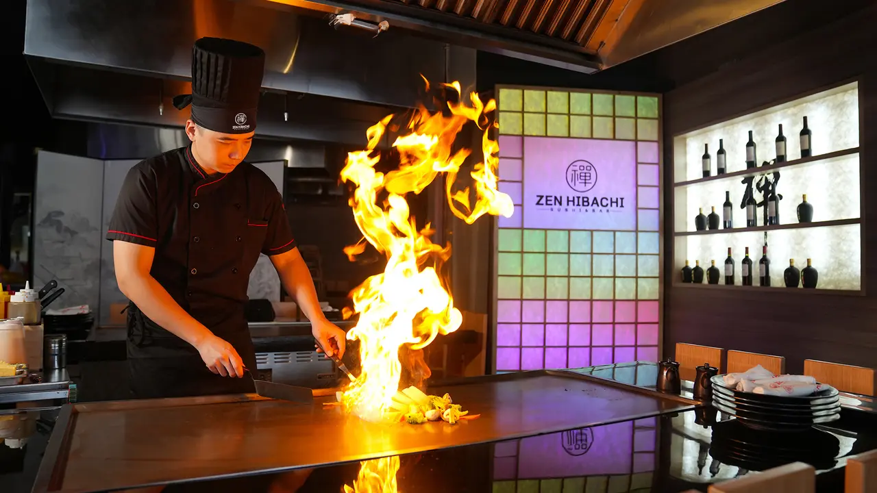 Chef performing flaming hibachi tableside cooking with fire blazing above counter in modern restaurant interior