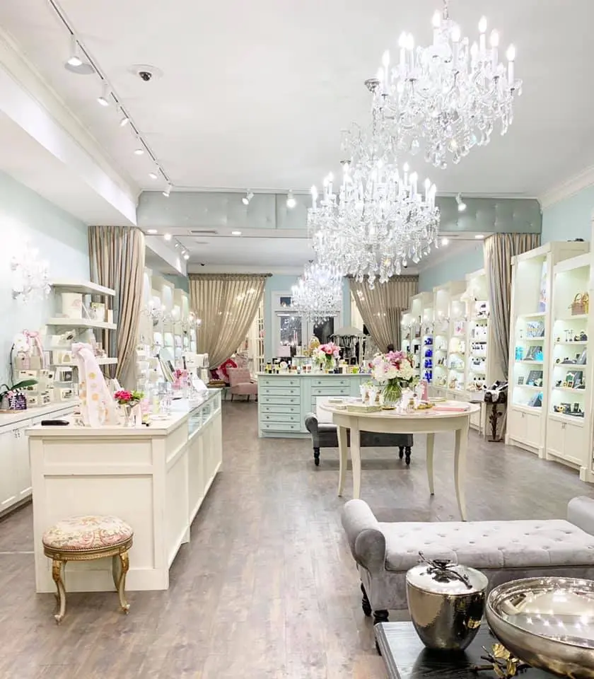 Luxury beauty boutique interior with crystal chandeliers, cream-colored display counters, beige curtains, and shelving displaying cosmetics and skincare