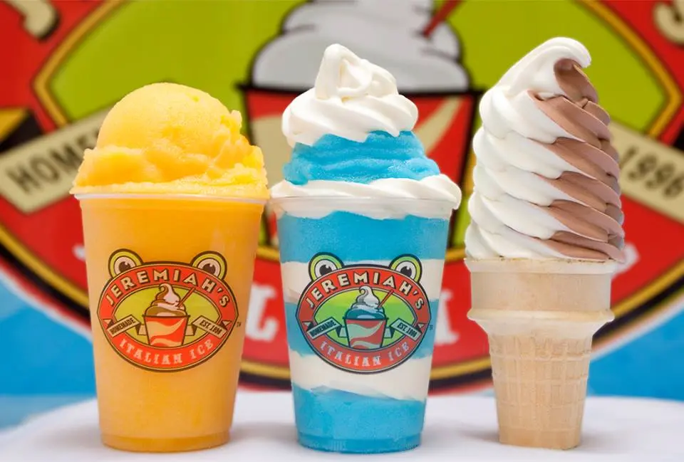 Three frozen desserts: yellow Italian ice with whipped cream in a branded cup, blue Italian ice with whipped cream in a branded cup, and vanilla soft serve in