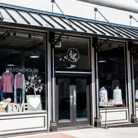 Storefront with black metal roof, large windows displaying pink clothing and home decor items, entrance doors with "Willow House" signage