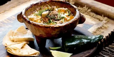 Creamy soup in a clay bowl with tortillas and lime wedges on the side