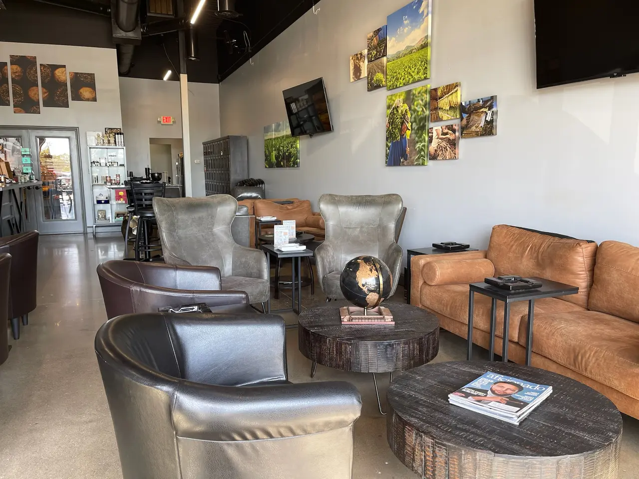 Interior lounge with gray and tan leather seating, dark wood tables, and framed landscape photographs on white walls