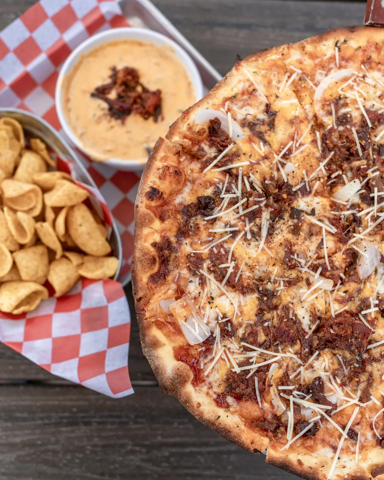 Wood-fired pizza topped with shredded meat and cheese, served with cashews and a creamy dipping sauce on checkered paper