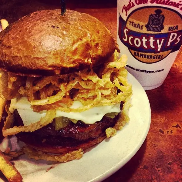 Hamburger with crispy onion strings and melted cheese on toasted bun, served with branded cup on white plate