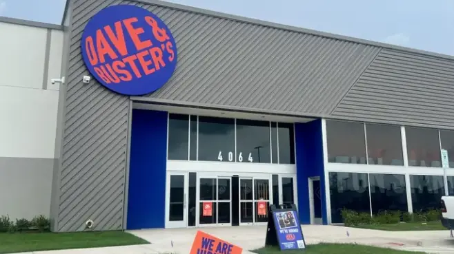 Exterior of Dave & Buster's building with illuminated circular logo, blue entrance doors, and large storefront windows
