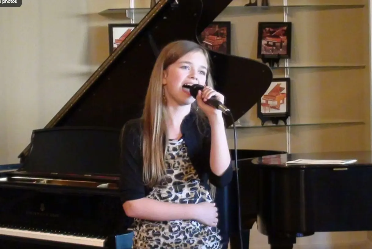 Young woman singing into microphone in front of grand piano in music studio