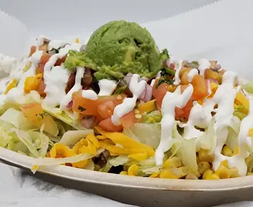 Taco salad with shredded lettuce, corn, black beans, diced tomatoes, white crema, and guacamole on top, served on a white plate