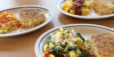 Golden hash browns and fluffy omelettes filled with vegetables served on white plates with blue trim