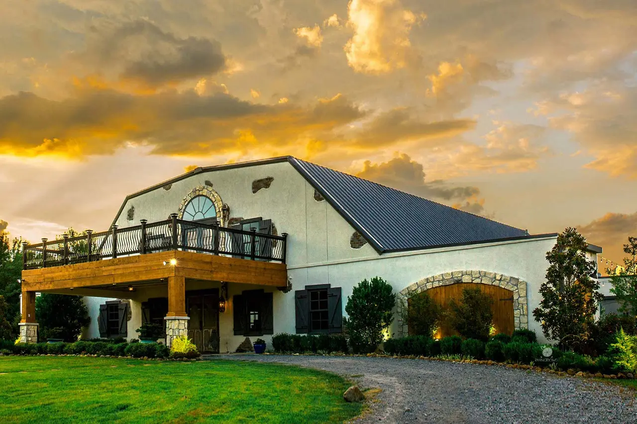 White barn-style building with upper deck and arched stone entrance, illuminated by golden sunset sky