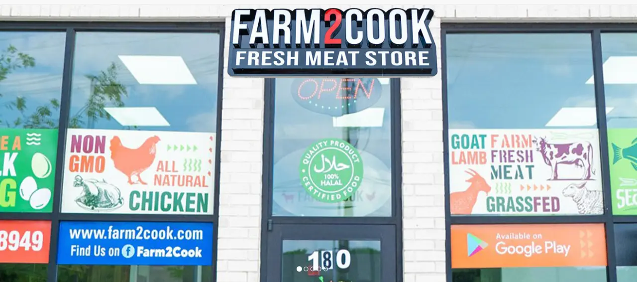 Storefront window of fresh meat market with signage advertising non-GMO natural halal meats including goat, chicken, beef, lamb, and grassfed options