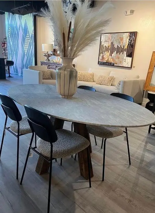 Oval marble dining table with black chairs and woven seats, tall vase of pampas grass, cream sofa and framed artwork in bright showroom