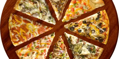 Six slices of different pizza varieties arranged in a circle on a wooden board, showing toppings including cheese, vegetables, and meats