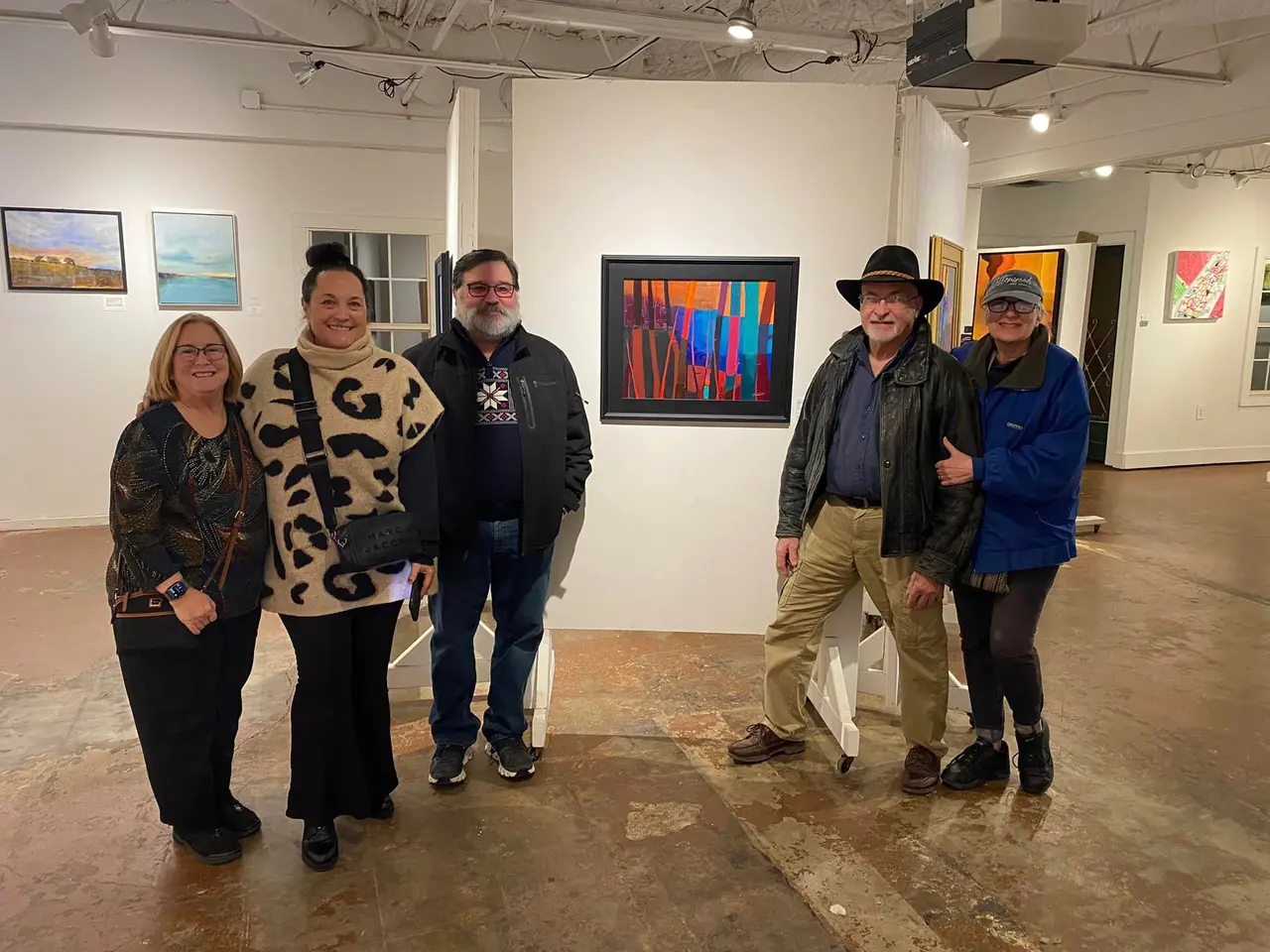 Five people standing in an art gallery with paintings hung on white walls