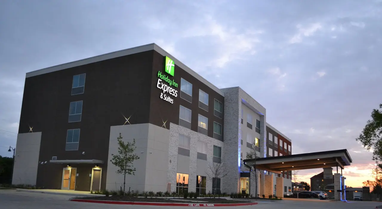 Modern hotel exterior with dark upper floors and white base, illuminated entrance, and covered parking area at dusk