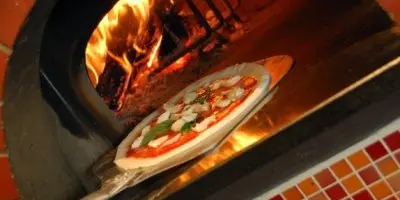 Pizza with toppings on wooden peel inside wood-fired oven with flames