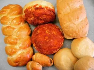Assorted baked goods including croissants, round bread rolls, braided loaves, and small pastries arranged on a white surface