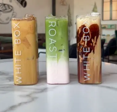 Three tall beverages in branded cups: tan-colored iced coffee, green matcha drink, and dark cola with ice