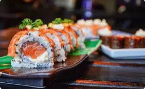 Sushi rolls topped with orange roe arranged on a black rectangular plate with green garnish