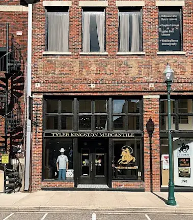 Red brick storefront with dark windows and entrance displaying men's clothing and merchandise on display