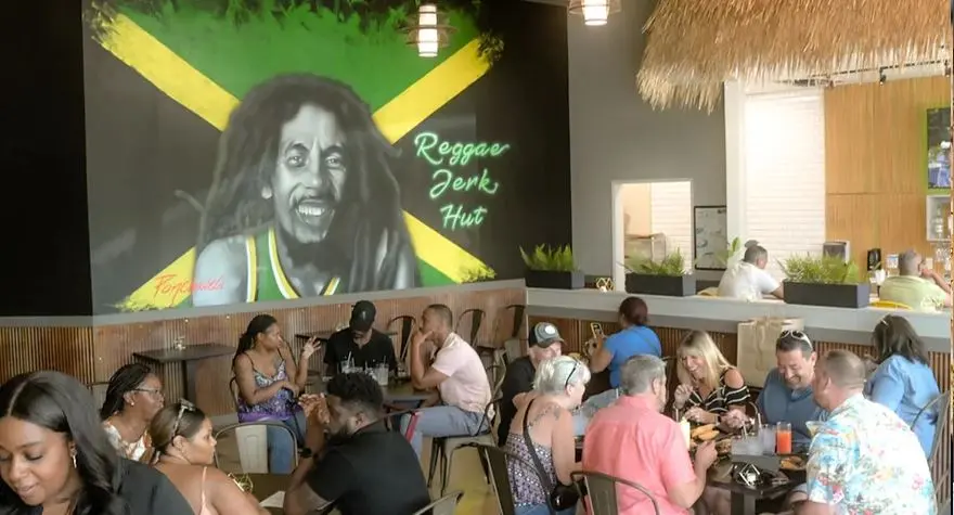 Interior of casual dining restaurant with customers seated at tables, large portrait mural on wall, thatched roof accent, and warm lighting