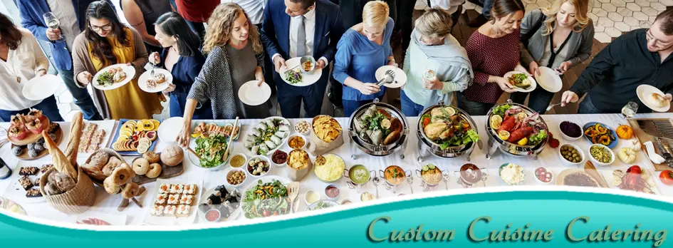 Overhead view of people standing around a long table laden with salads, grilled meats, breads, and various prepared dishes