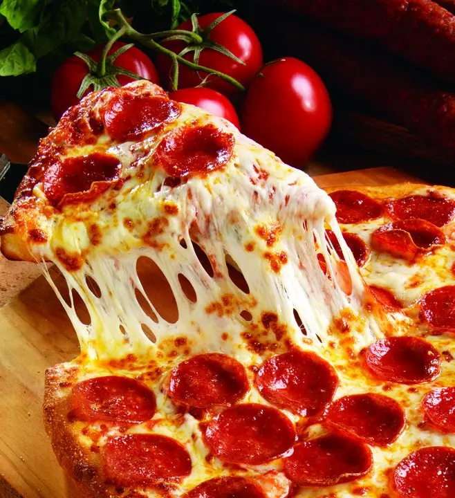 Pepperoni pizza with melted cheese stretching, fresh tomatoes on vine in background