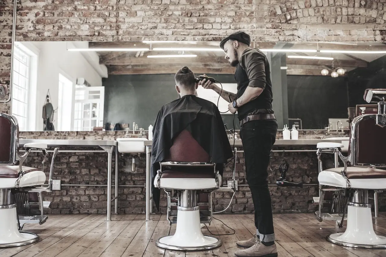 Barber cutting client's hair in industrial-style shop with exposed brick wall and vintage barber chairs