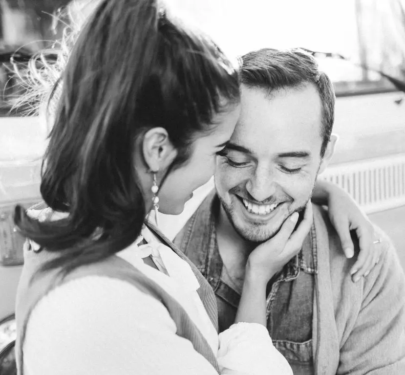Woman whispering to smiling man in black and white portrait