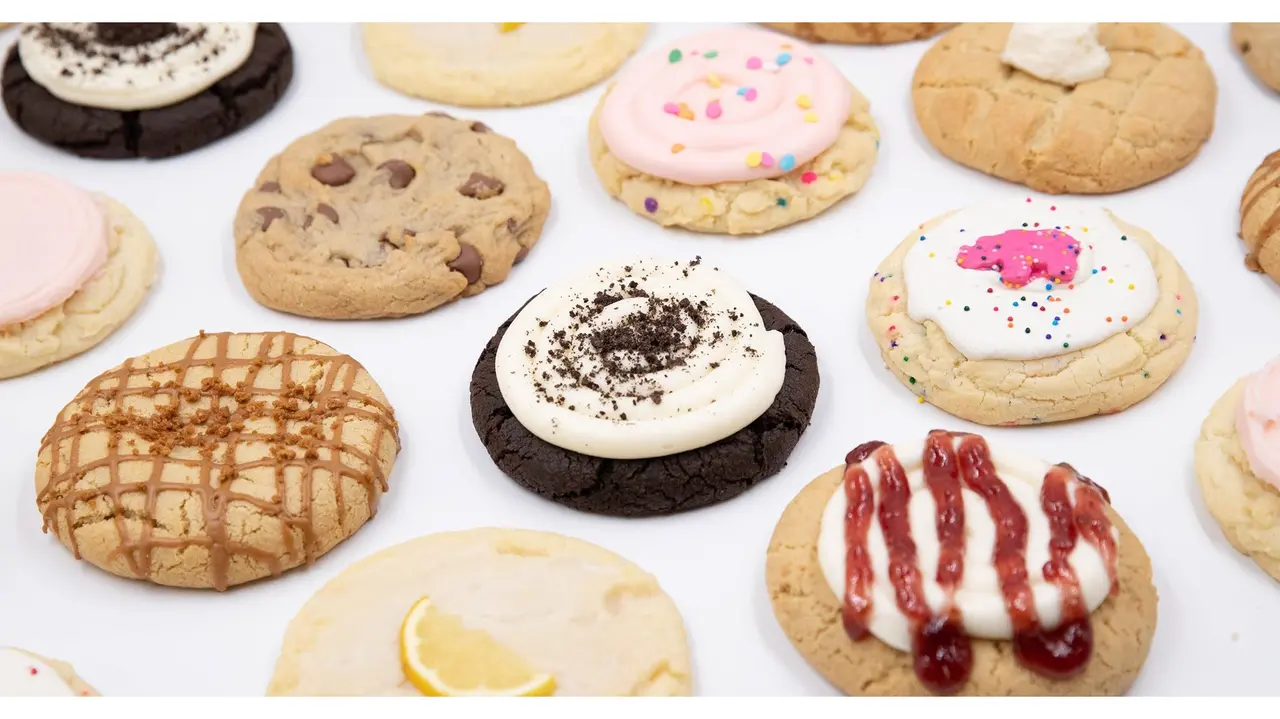 Assorted decorated cookies including chocolate chip, frosted, and drizzled varieties arranged on white surface