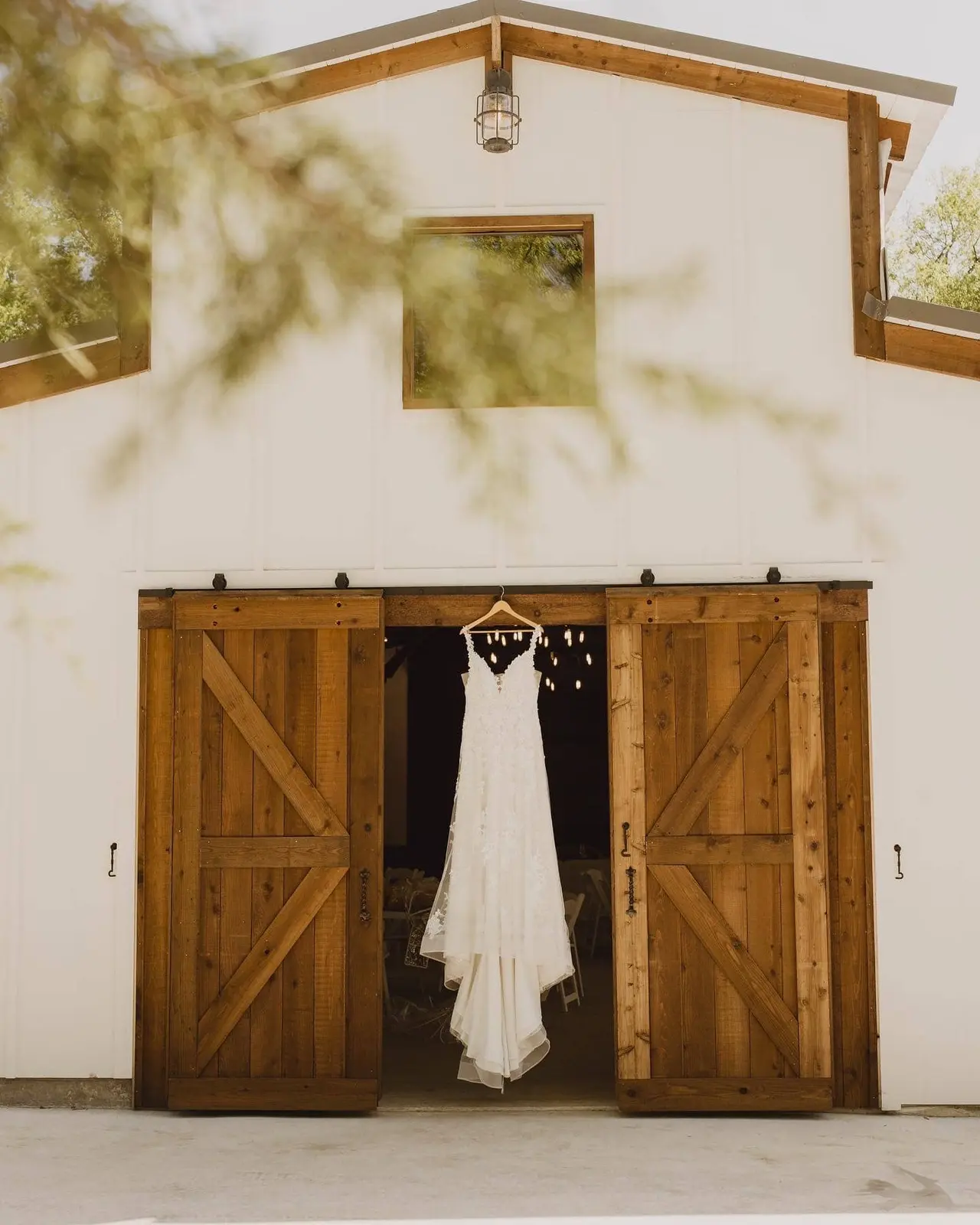 White wedding dress hanging from barn door frame with wooden X-panel sliding doors open