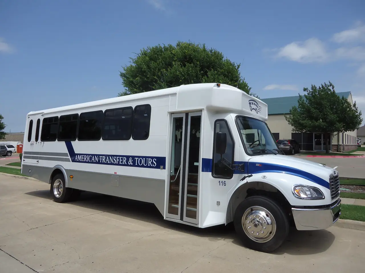 White and blue passenger shuttle van parked on pavement with trees in background