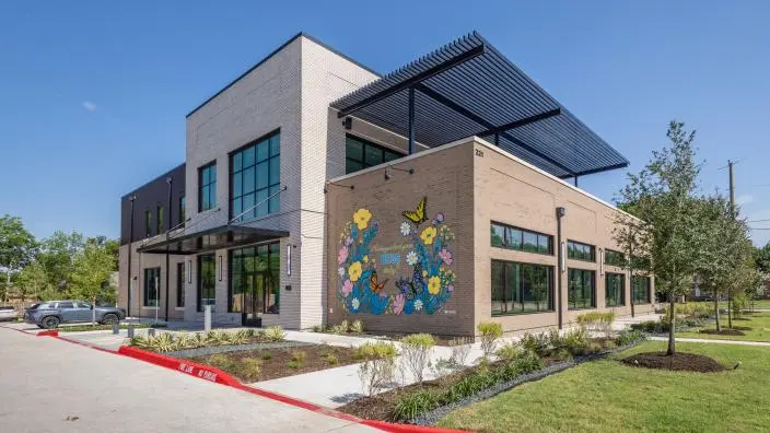 Modern building with brick and stone exterior, large windows, and colorful mural on facade, landscaped grounds with red painted pathway