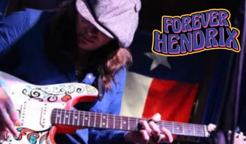 Musician playing electric guitar with decorative artwork on body, wearing blue shirt and light-colored head wrap