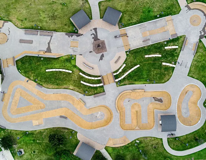 Aerial view of skatepark with curved concrete bowls, ramps, and smooth riding surfaces surrounded by green grass and seating areas