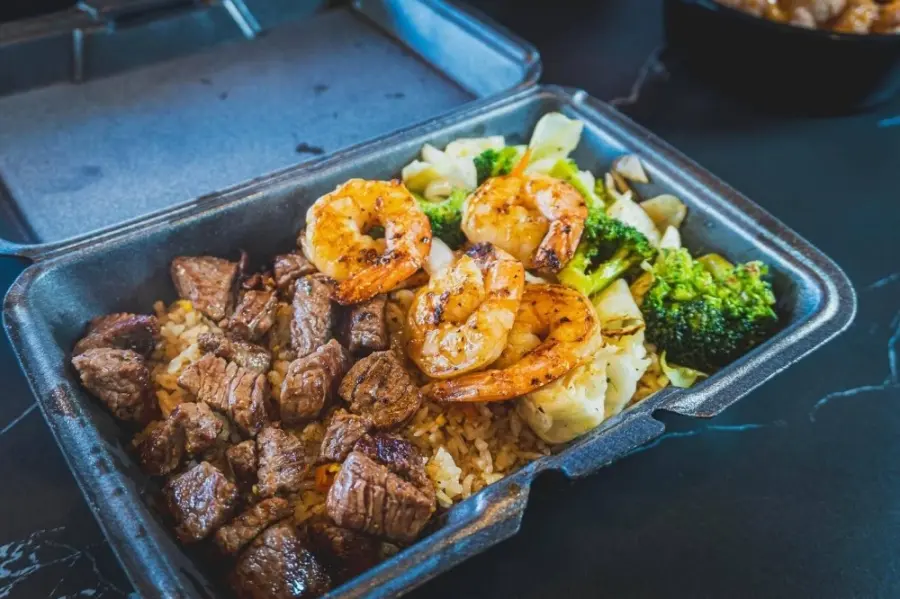 Grilled steak, shrimp, potatoes, and broccoli in a takeout container