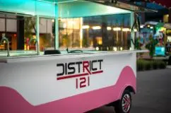 Pink and white food truck parked in front of illuminated indoor dining venue at dusk