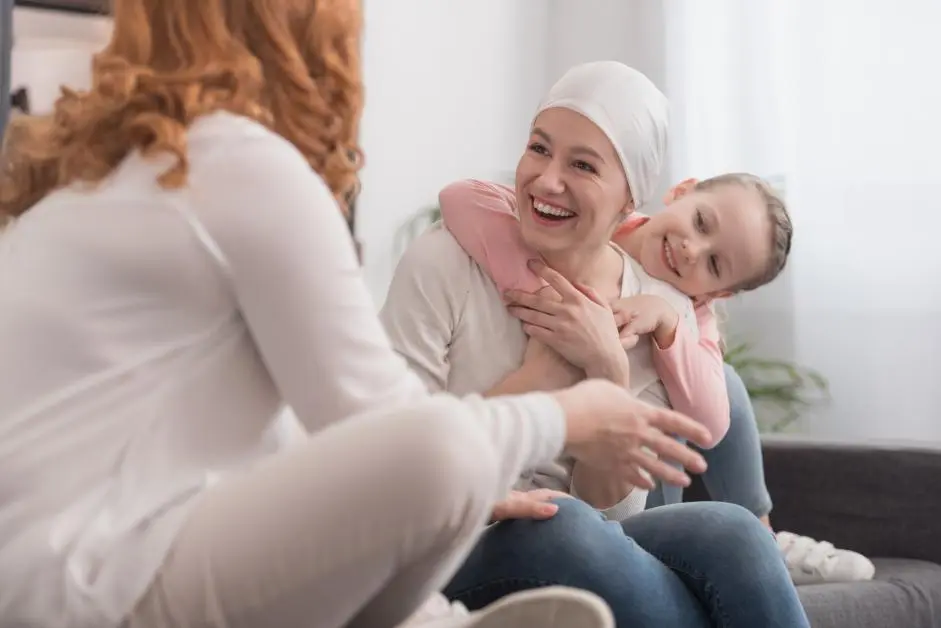 Woman wearing head wrap holding infant while smiling at another woman indoors