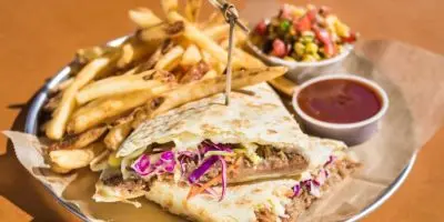 Quesadilla with shredded purple cabbage served with golden fries and red sauce on a round plate