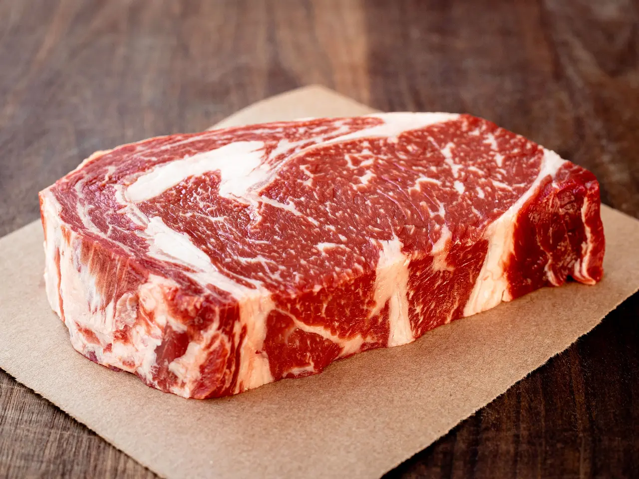 Raw marbled beef steak on parchment paper against a wooden surface