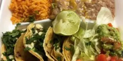 Plated tacos with shredded chicken, lettuce, and toppings, served with rice and refried beans